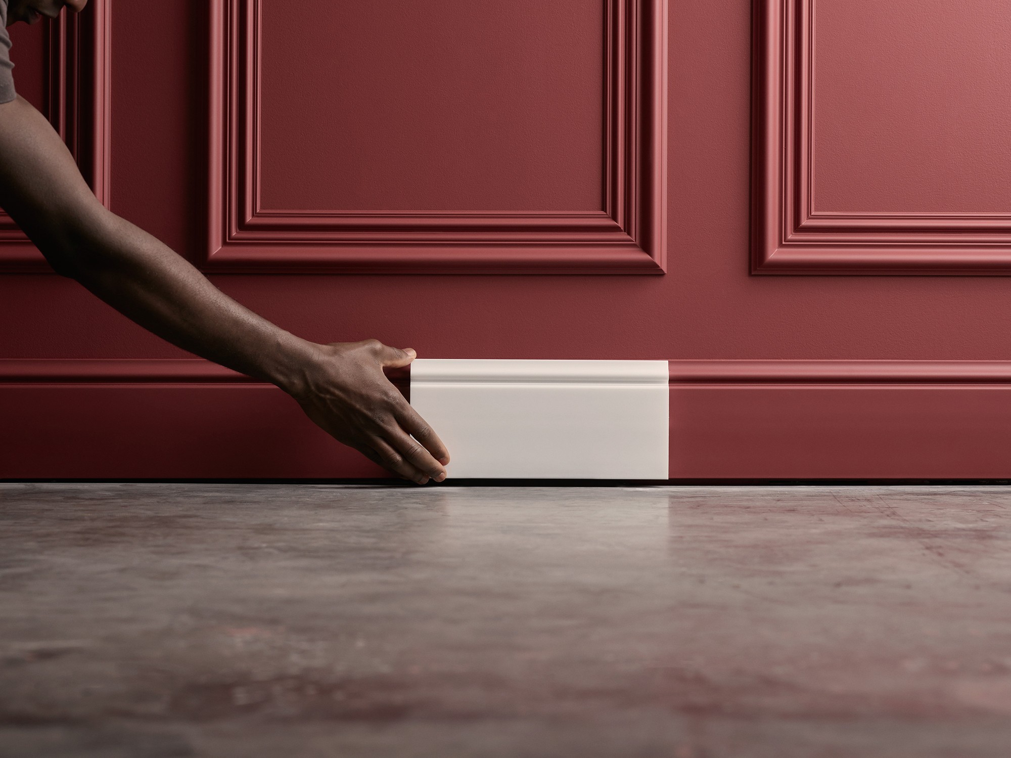 ORAC Eine Hand hält eine Sockelleiste vor eine Wand